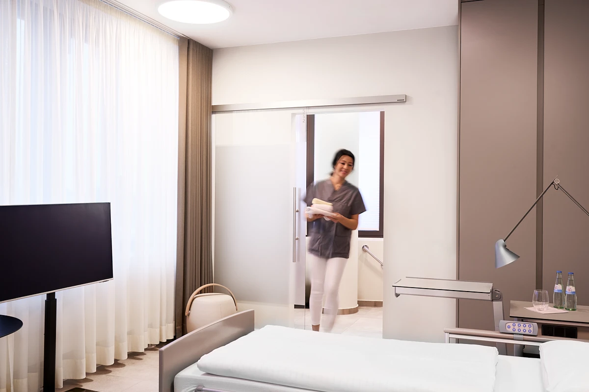 Modernes Patientenzimmer der RKM 740 Facharztklinik in Düsseldorf mit Pflegekraft, Einzelbett, TV und integriertem Bad