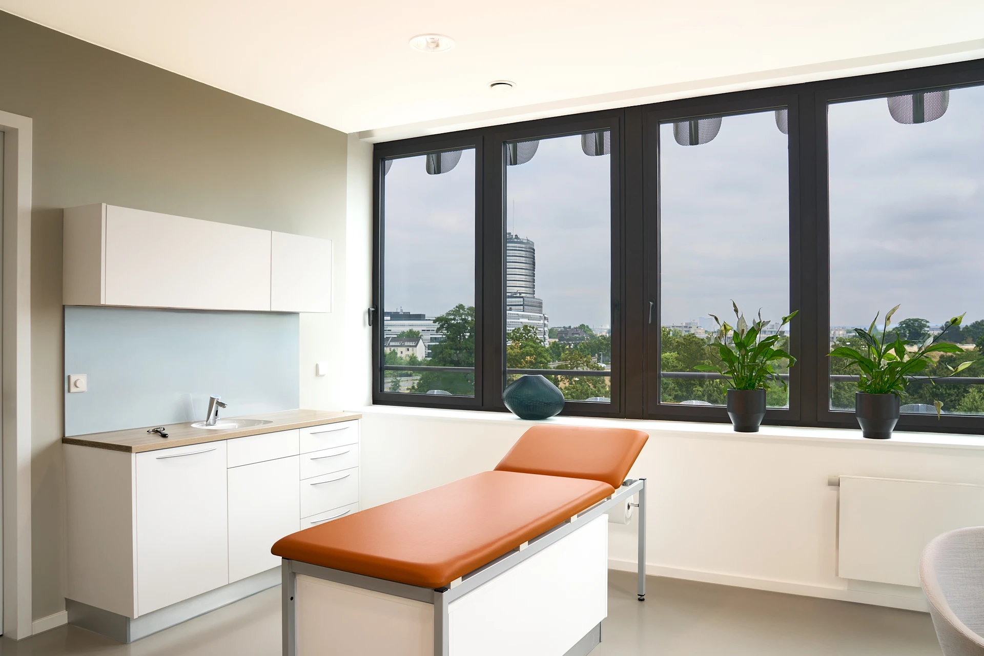 Behandlungszimmer der RKM 740 Wirbelsäulen- und Neurochirurgie Behandlungszimmer der RKM 740 Wirbelsäulen- und Neurochirurgie in Düsseldorf mit Untersuchungsliege und Blick über die Stadt