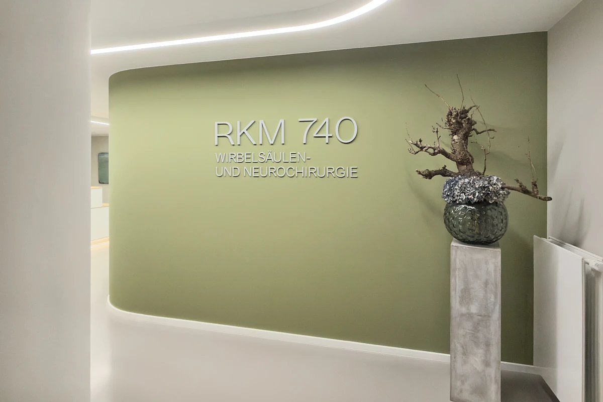 Praxiswand mit Schriftzug der RKM 740 Wirbelsäulen- und Neurochirurgie und floralem Arrangement in Düsseldorf